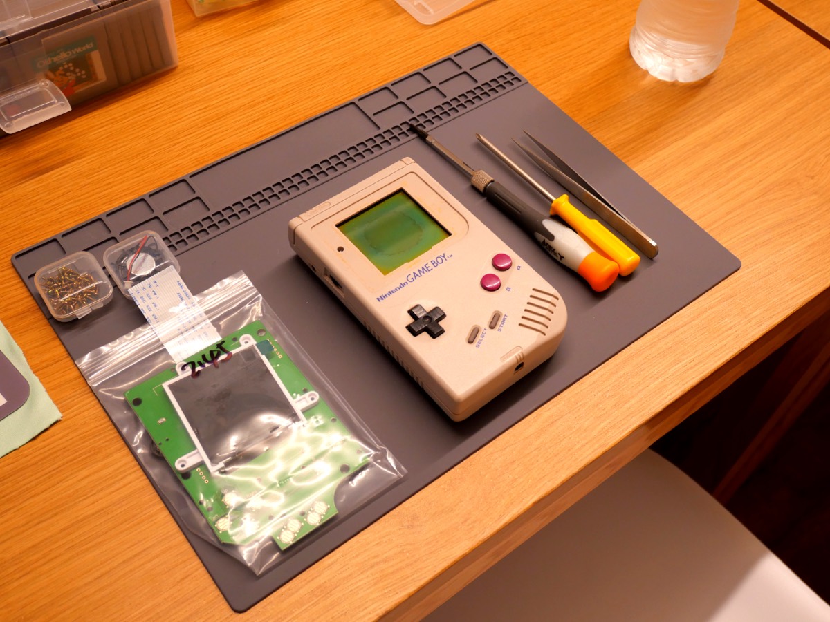 A vintage Game Boy, its board and tools laid out on the work mat, ready to begin