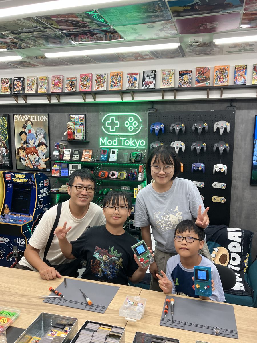 A family of four flashing peace signs with their finished Game Boys under the Mod Tokyo neon sign
